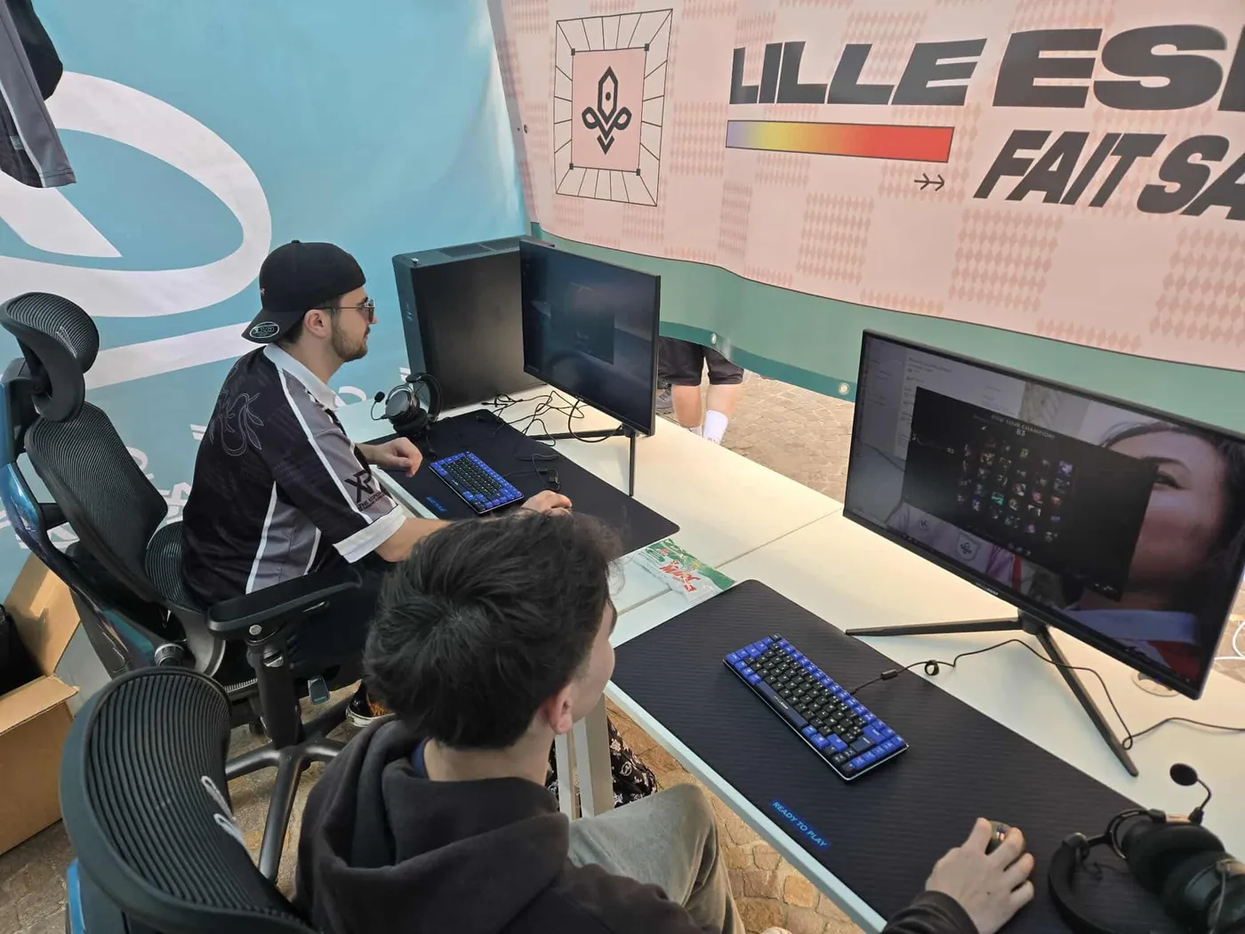 Sous la tente du club, deux joueurs sur des postes PC devant la banderole Lille Esport fait sa braderie.