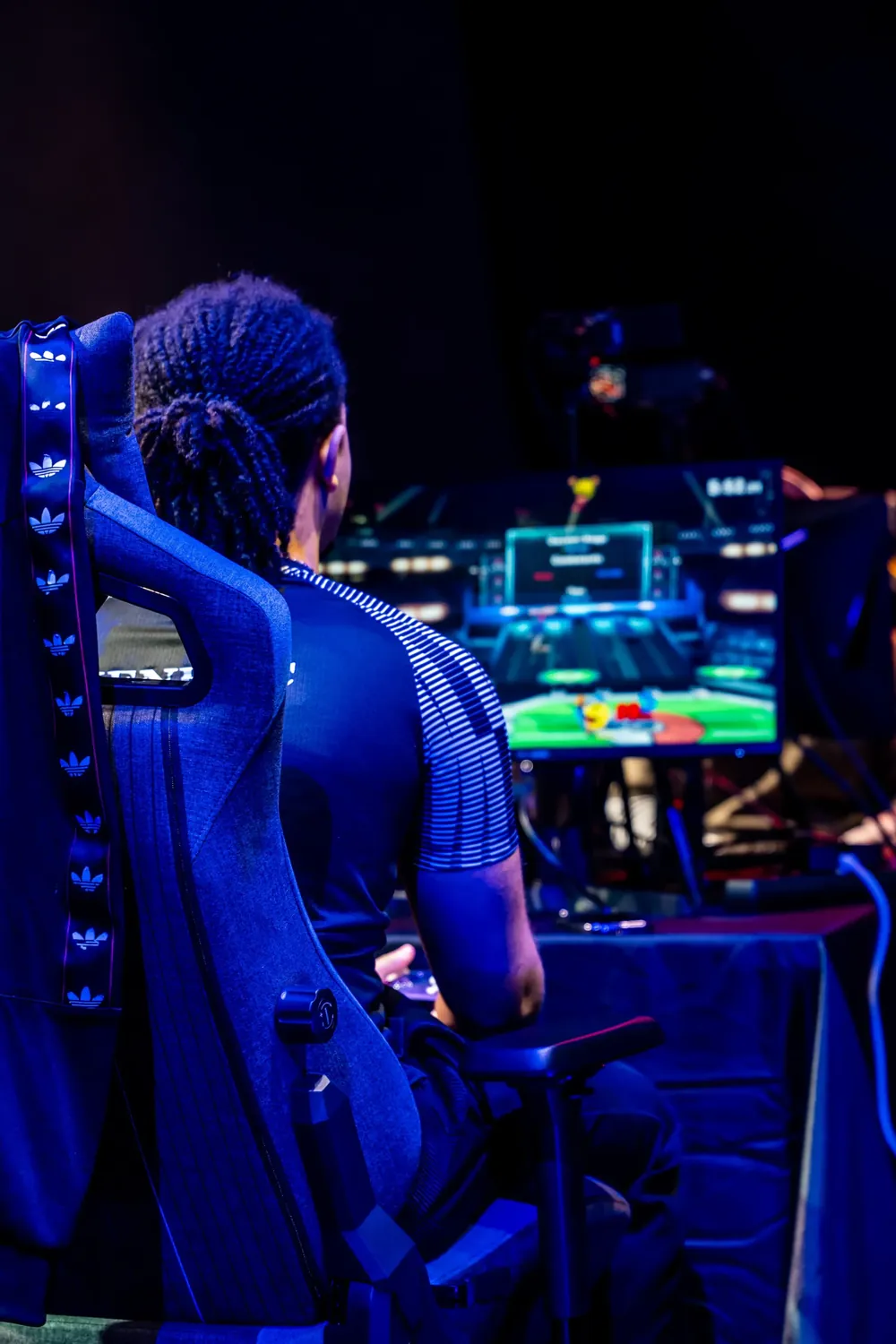 Un joueur de dos dans un fauteuil gaming, face à l'écran, sous une lumière bleue.