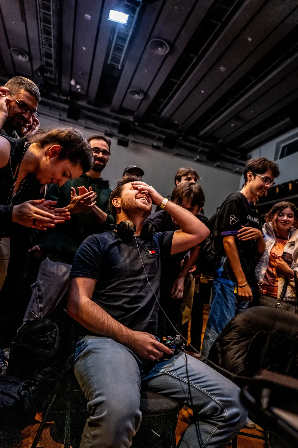 Un joueur rit, la main sur les yeux, entouré de spectateurs qui applaudissent.