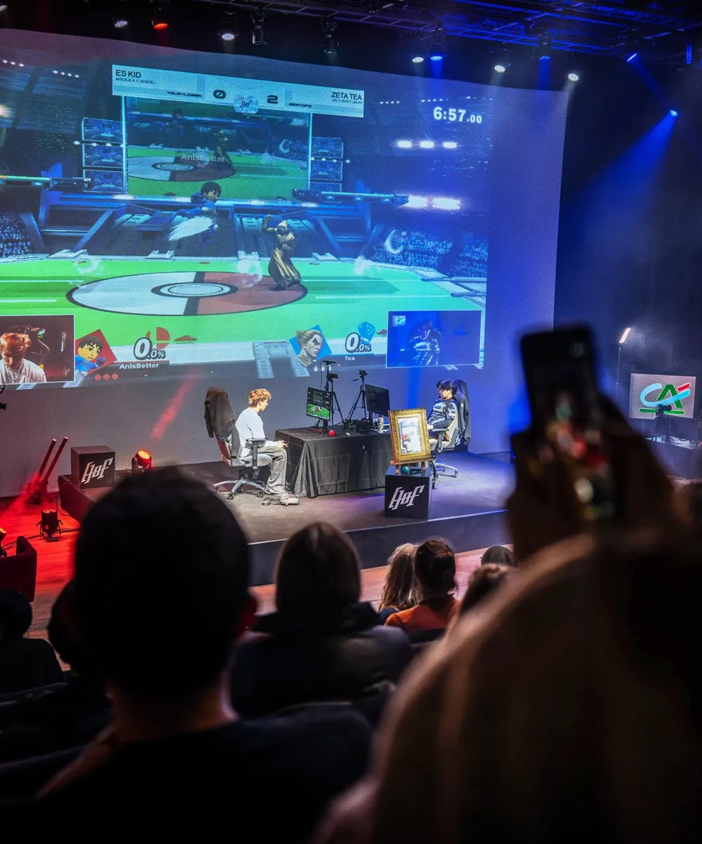 Deux joueurs sur scène face à un écran géant qui diffuse le match de Super Smash Bros.